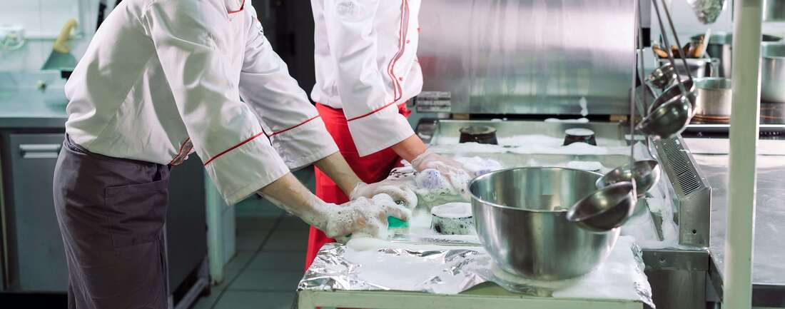 2 people cleaning the stainless steel surfaces in a commercial kitchen
