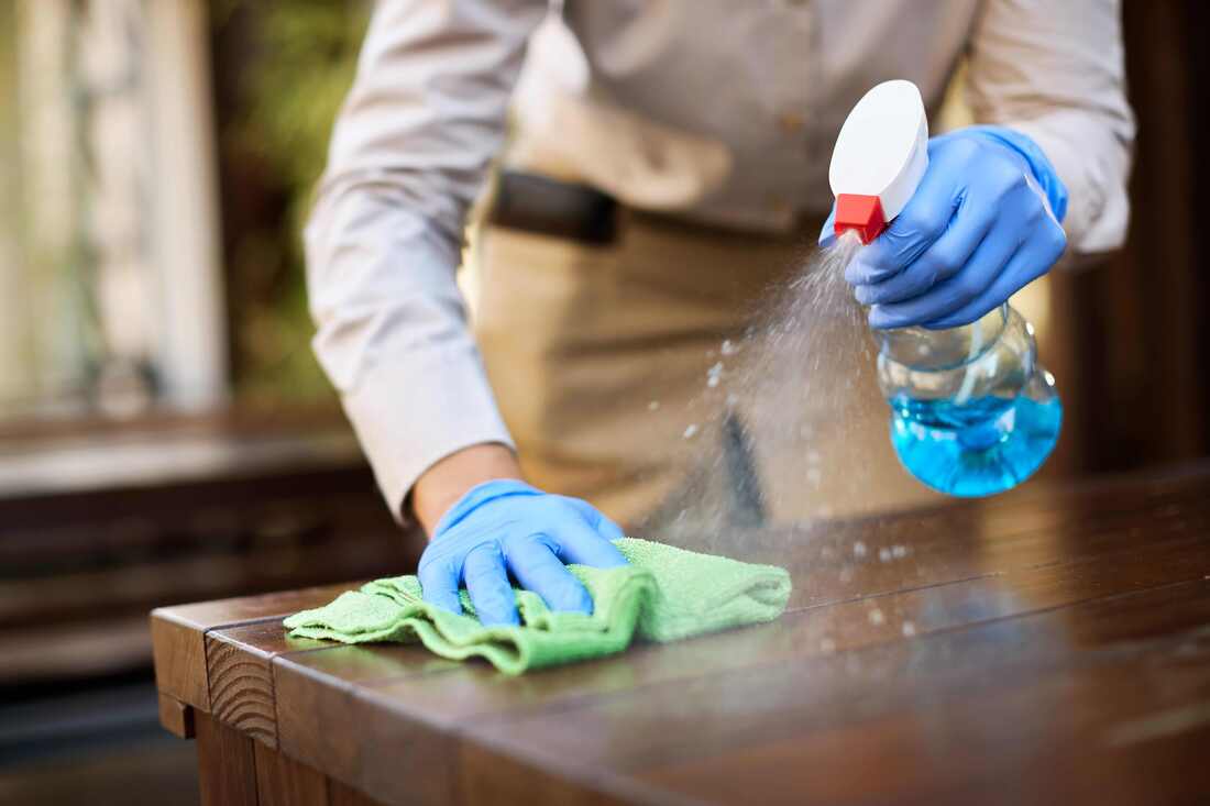 Man spraying a cleaning compound on a table and wiping it off with a towel